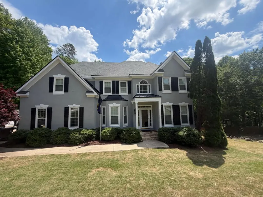 Grey two-story house with white trim and black shutters after exterior painting